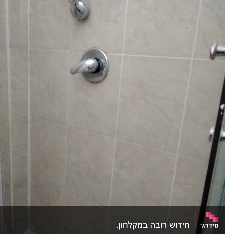 ברז מקלחת עם ידית מתכת על קיר אריחים